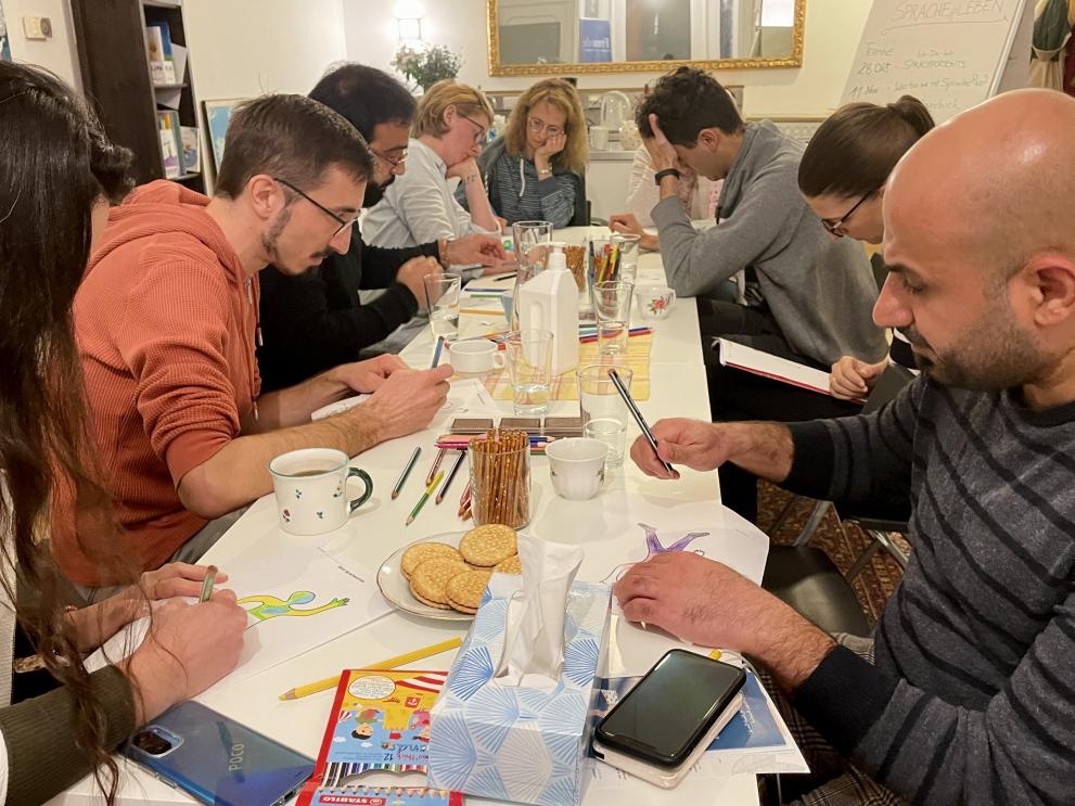 A photo of adulsts drawing and colouring together on a big table.